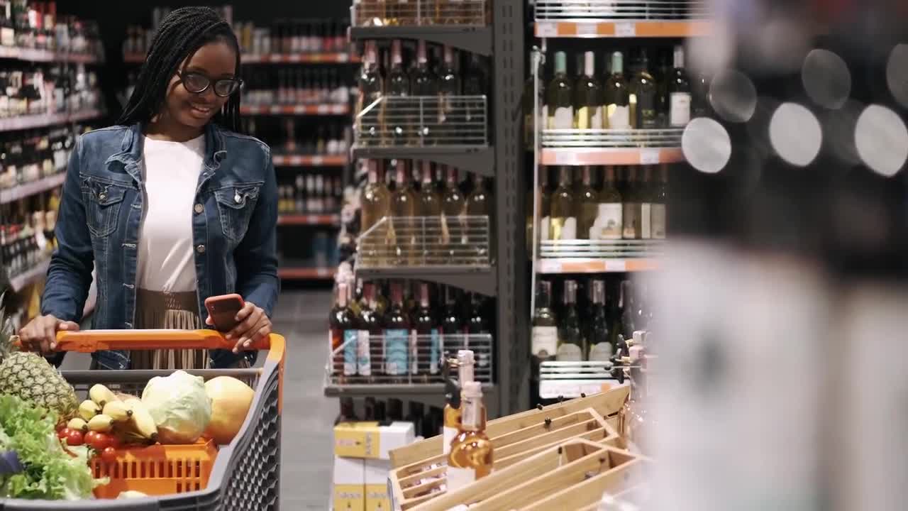 A shopper with a full cart checking her phone in a store aisle